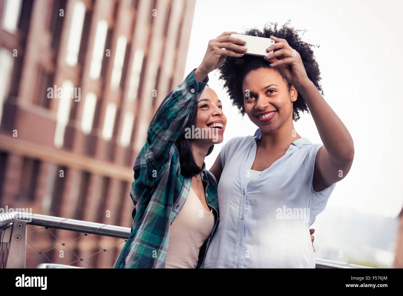 Due donne in posa e prendendo un selfie da un grande edificio nella città Foto Stock