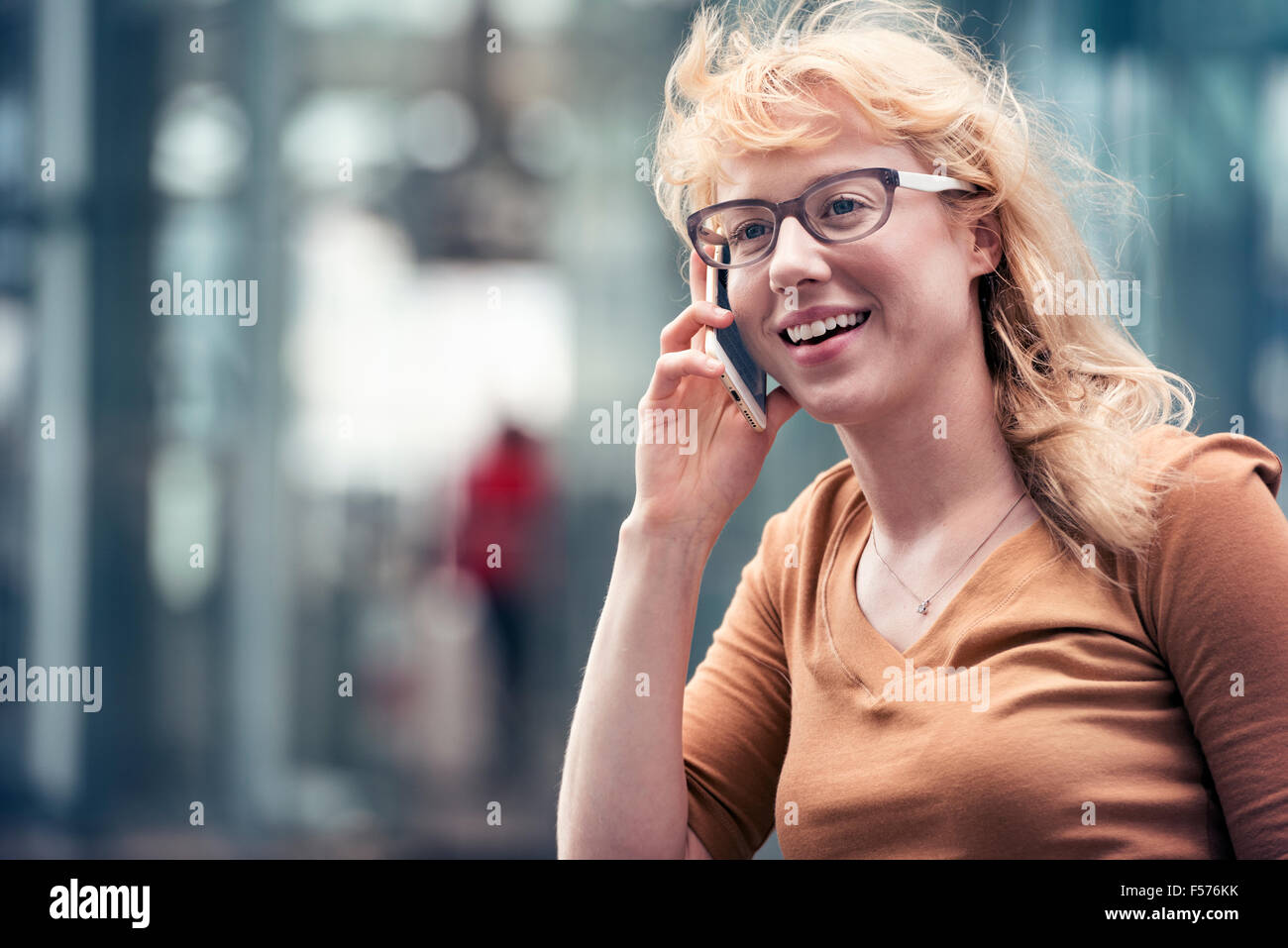 Una donna bionda a parlare su un telefono cellulare su una strada della città Foto Stock