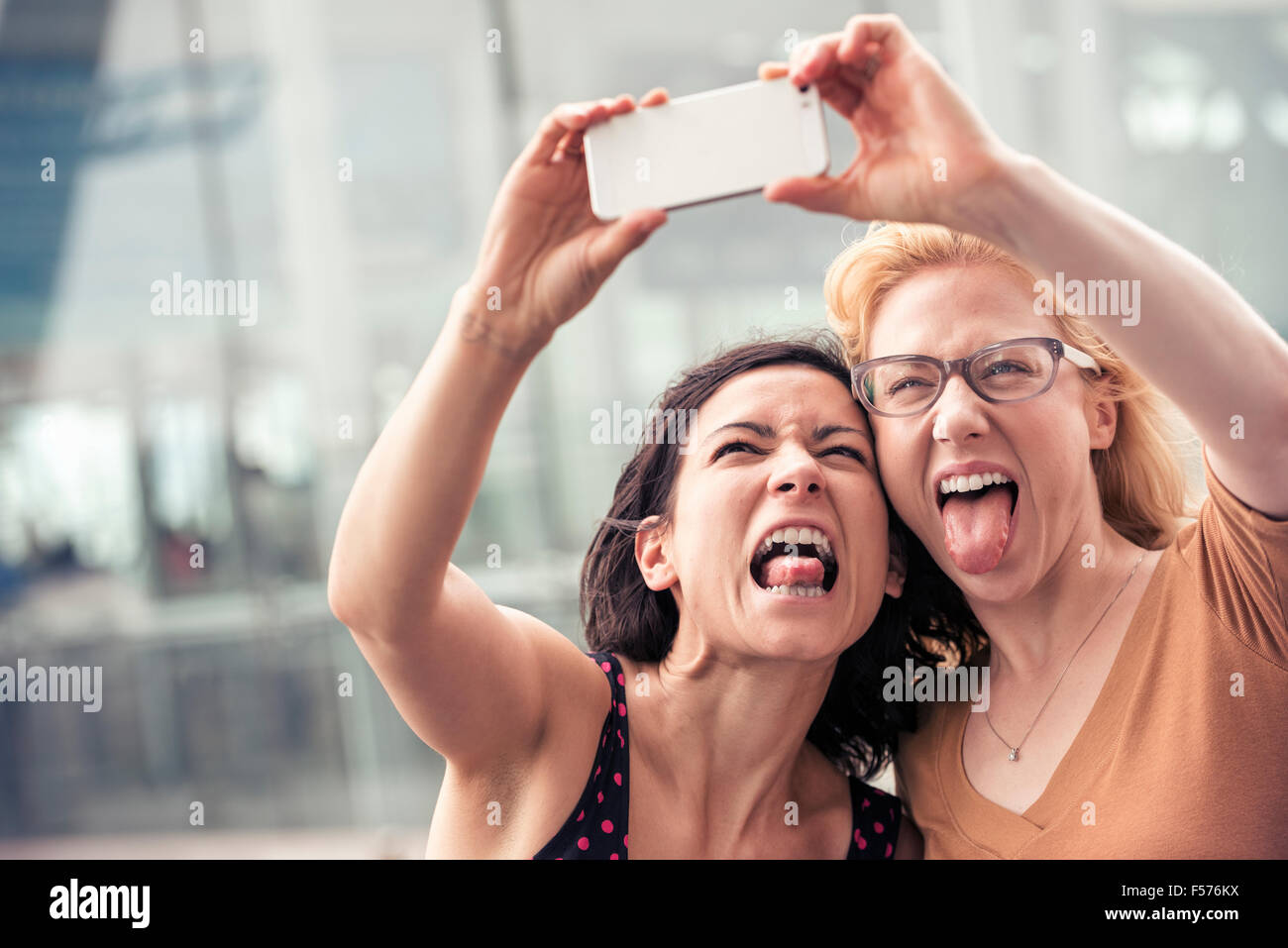 Due donne su una strada di città, prendendo un selfie con uno smart phone. Foto Stock