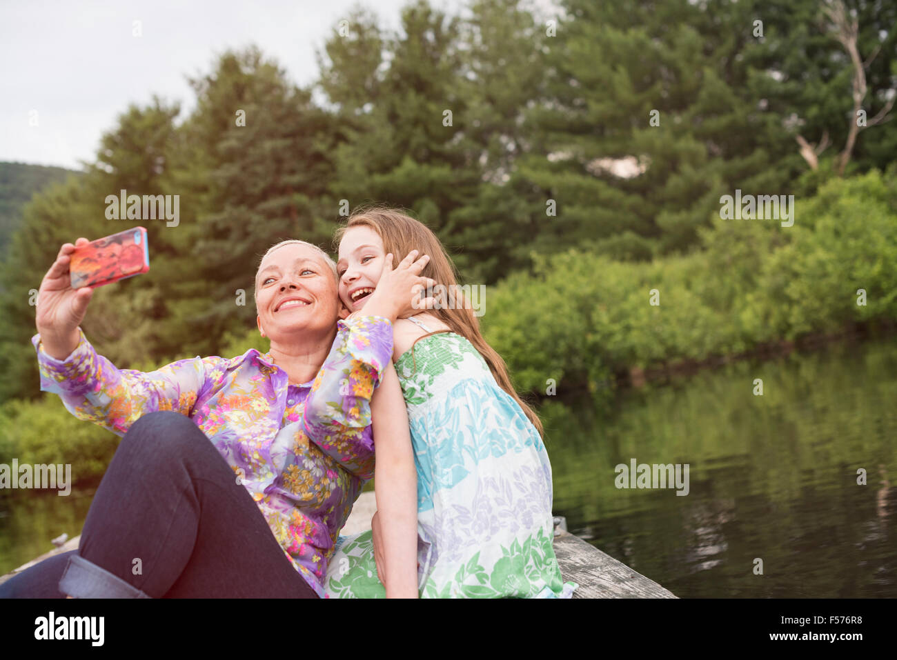Una donna e un bambino seduto su un lago dock tenendo un selfie con uno smart phone. Foto Stock