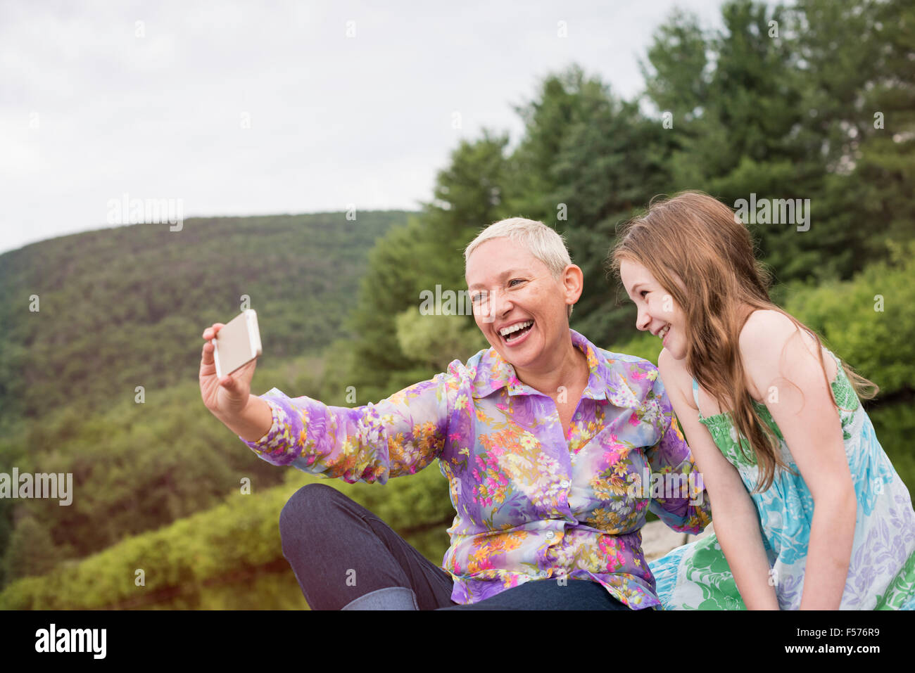 Una donna e un bambino seduto su un lago dock tenendo un selfie con uno smart phone. Foto Stock