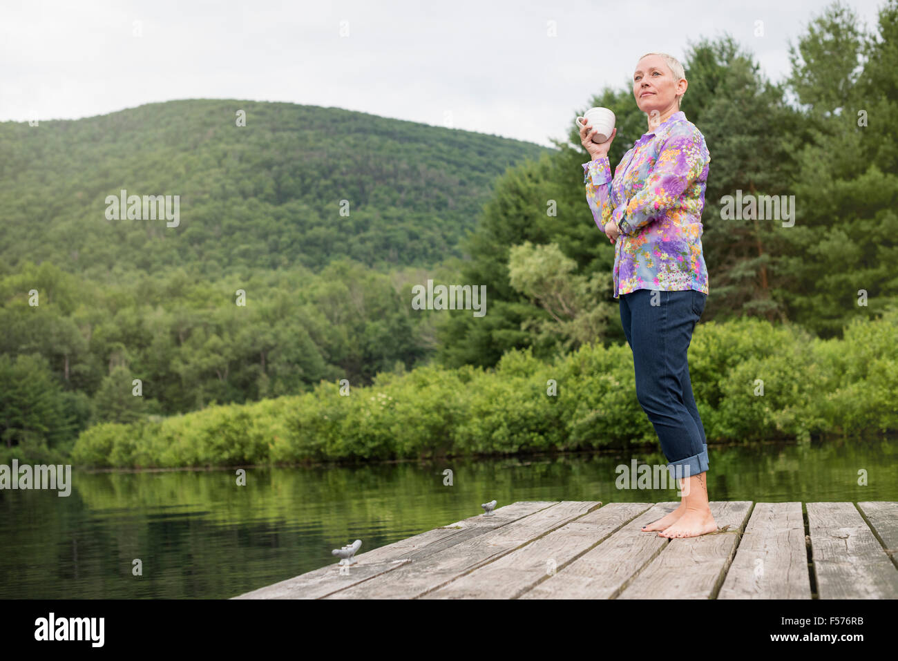 Una donna in piedi su un lago dock tenendo una tazza di caffè. Foto Stock