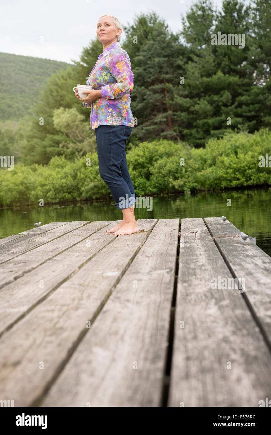 Una donna in piedi su un lago dock tenendo una tazza di caffè. Foto Stock