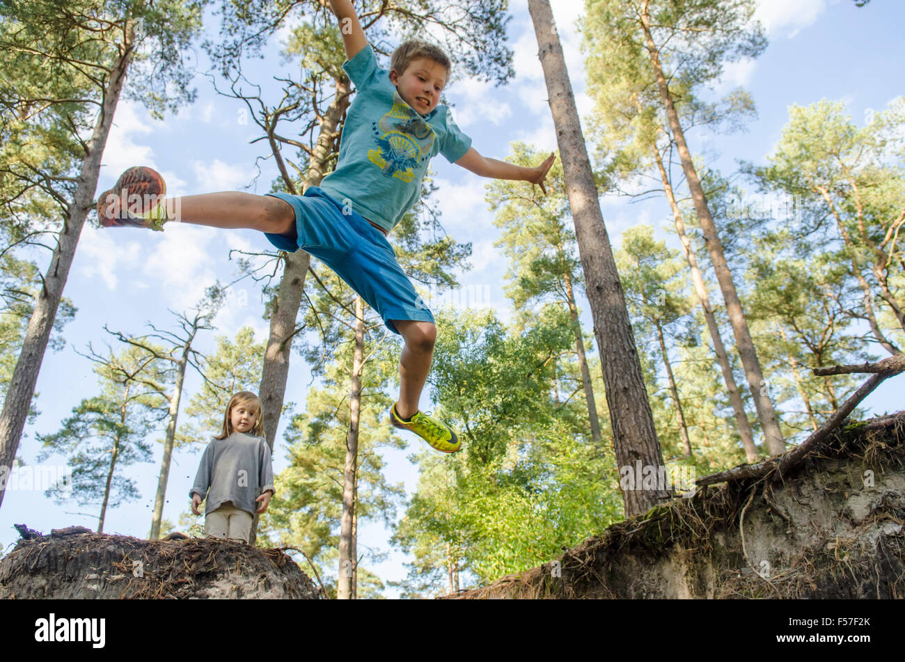 Bambino di nove anni facendo salti di star fuori da una banca con i suoi tre anni suor guardando nel bosco, Sussex. Regno Unito. Ottobre. Foto Stock