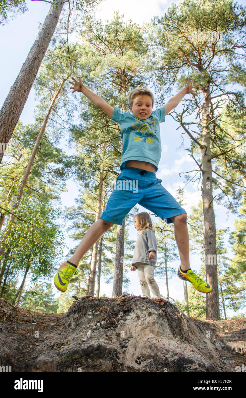 Bambino di nove anni facendo salti di star fuori da una banca con i suoi tre anni suor guardando nel bosco, Sussex. Regno Unito. Ottobre. Foto Stock