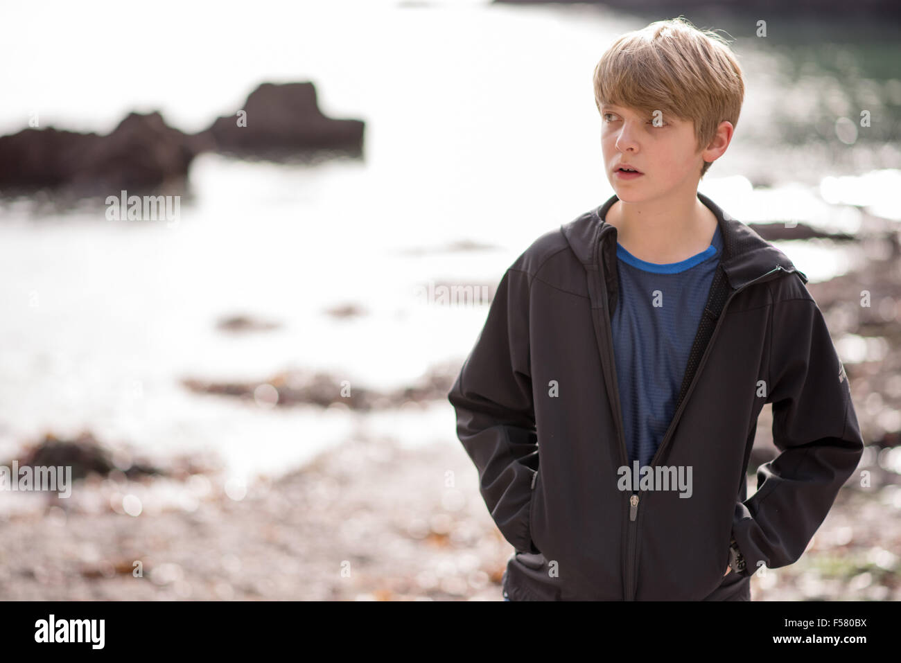 Biondo bianco ragazzo adolescente in una giacca nera cammina da sola su una spiaggia cercando triste e infelice in autunno sunshine Foto Stock