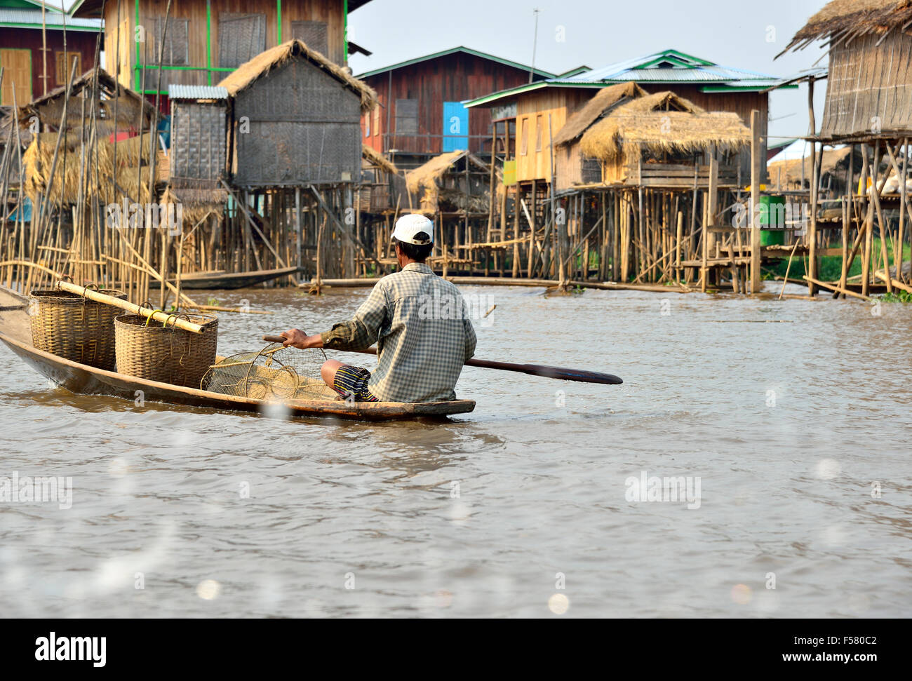 La minoranza etnica Intha fisheman paddling piccola canoa tipo barca lungo le vie navigabili tra palafitte, Lago Inle,Stato Shan,Myanmar Foto Stock