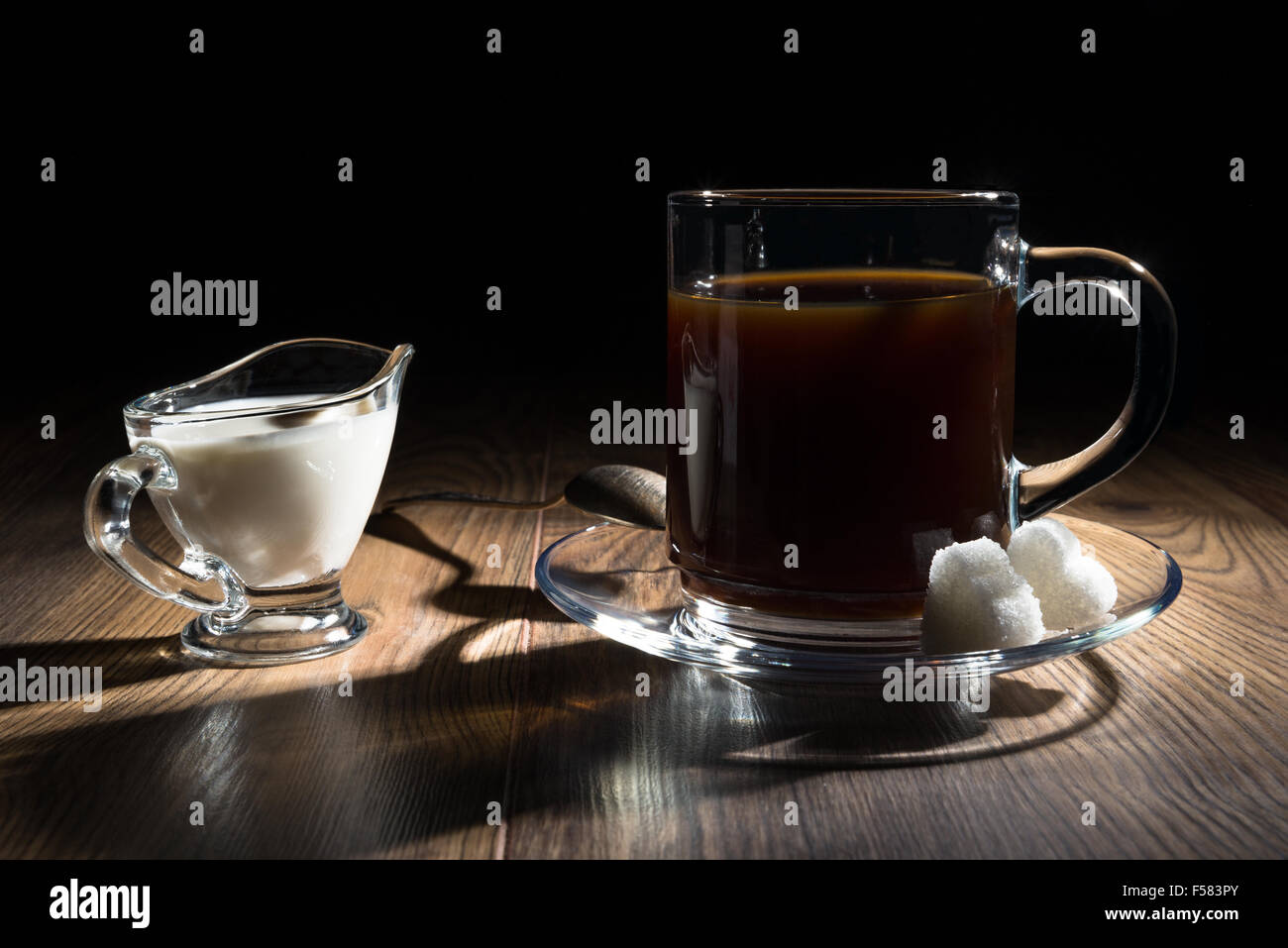 Un caffè in una tazza trasparente, latte, un cucchiaio di zucchero e Foto Stock