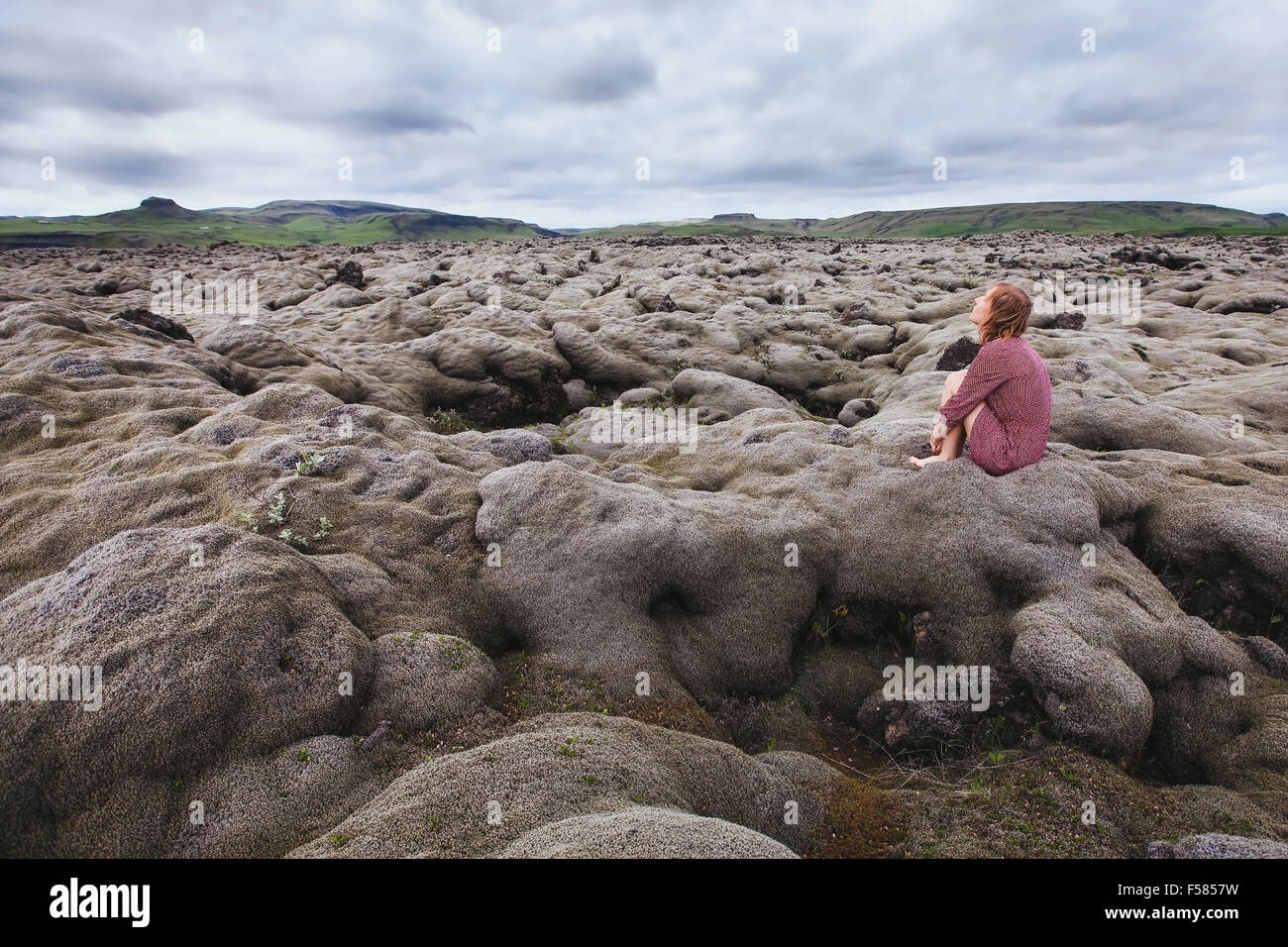 Donna seduta da sola nel campo di lava, guardando il cielo e il pensiero circa il significato della vita Foto Stock