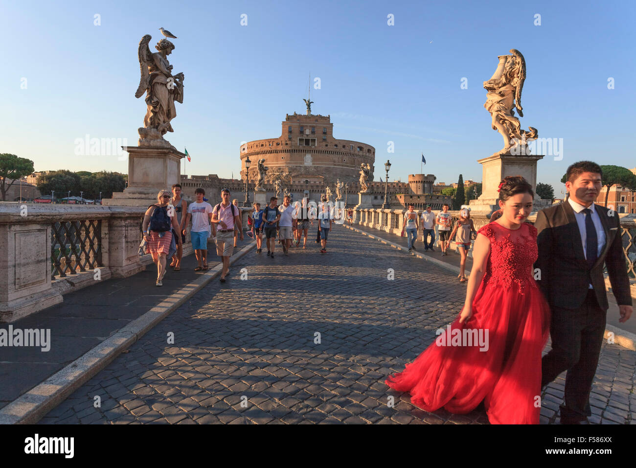 Pedoni croce camminare Sant'Angelo con ponte di Castel Santâ Angelo in background in un assolato pomeriggio estivo vicino al tramonto Foto Stock