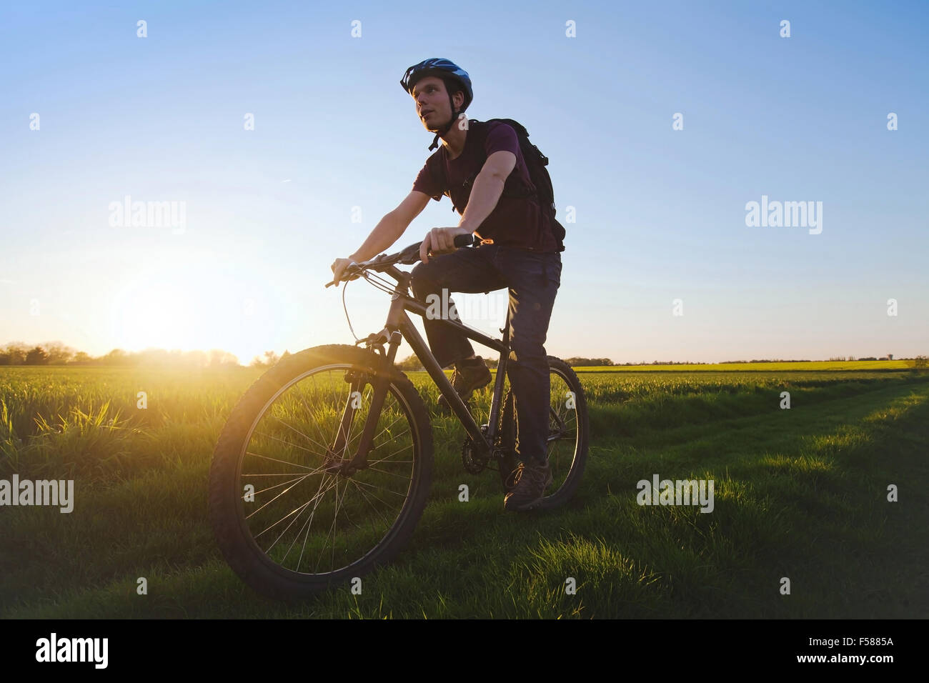 Giovane uomo sportivo equitazione bicicletta all'aperto al tramonto Foto Stock