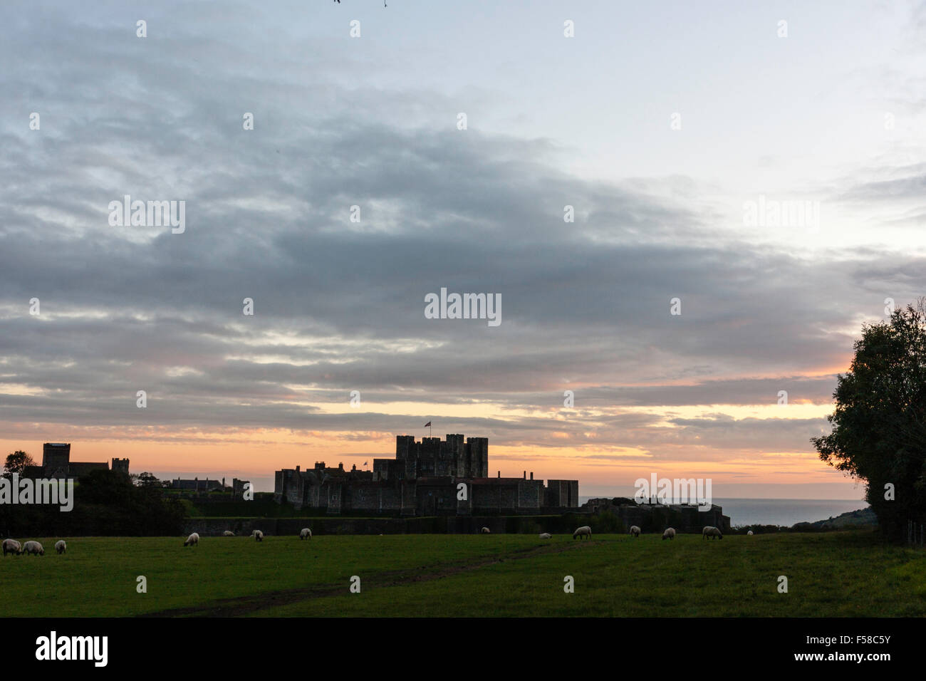 Inghilterra, il castello di Dover. Mantenere e pareti esterne profilarsi all'orizzonte con nuvoloso sera cielo arancione e il Canale della Manica in background. Foto Stock