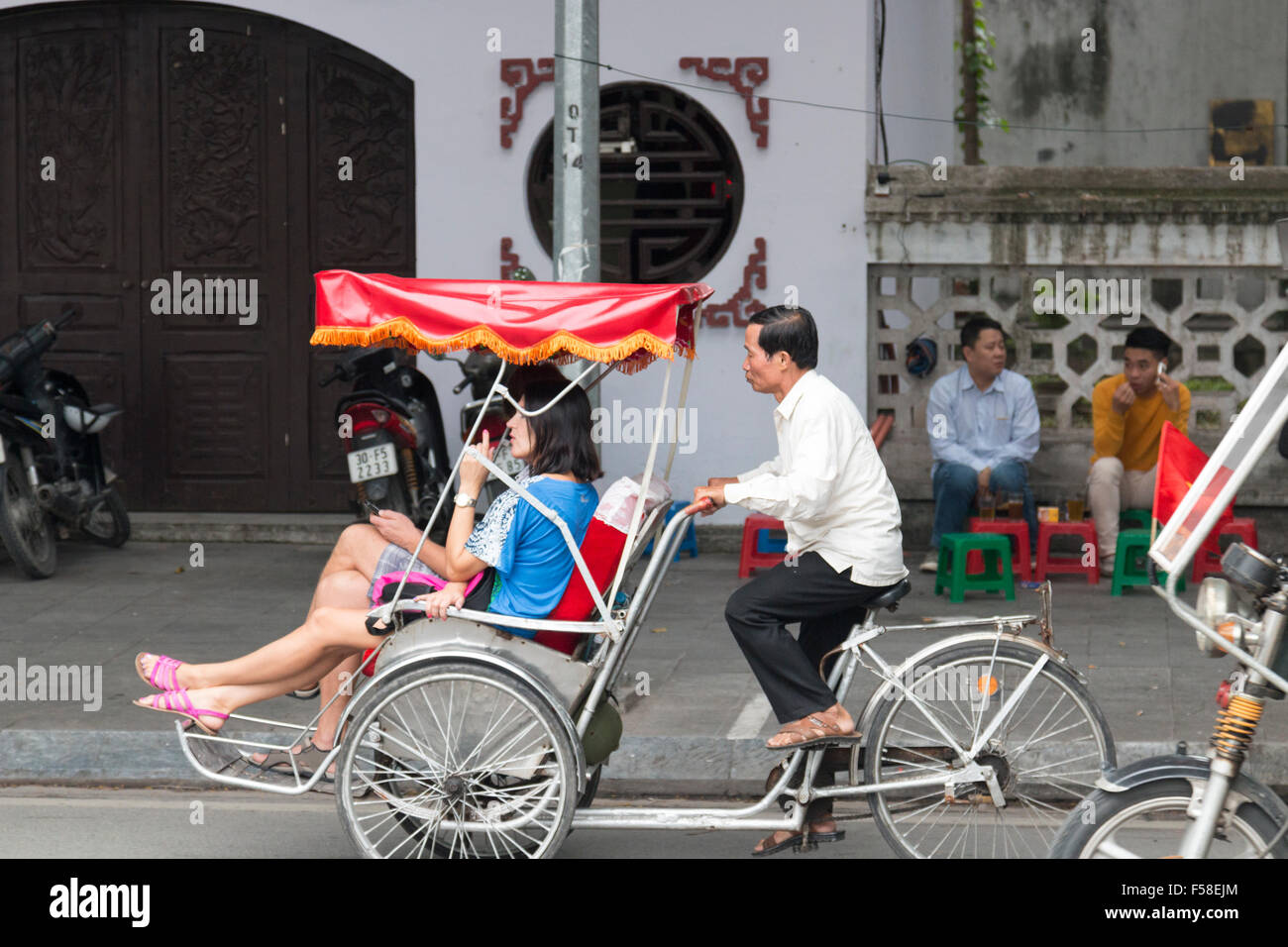 Maschio vietnamita in cyclo rickshaw rider il trasporto di due clienti attraverso le strade di Hanoi centro,Vietnam,asia Foto Stock