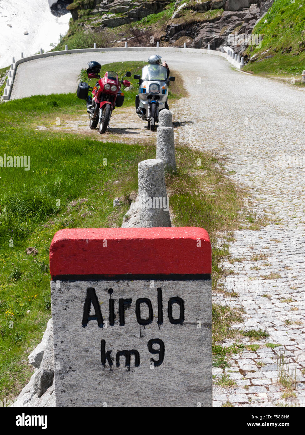 Due motociclette sono parcheggiate dietro una pietra miliare sulla storica di ciottoli lastricato in pietra San Gottardo pass road (Tremola) nelle alpi svizzere. Foto Stock