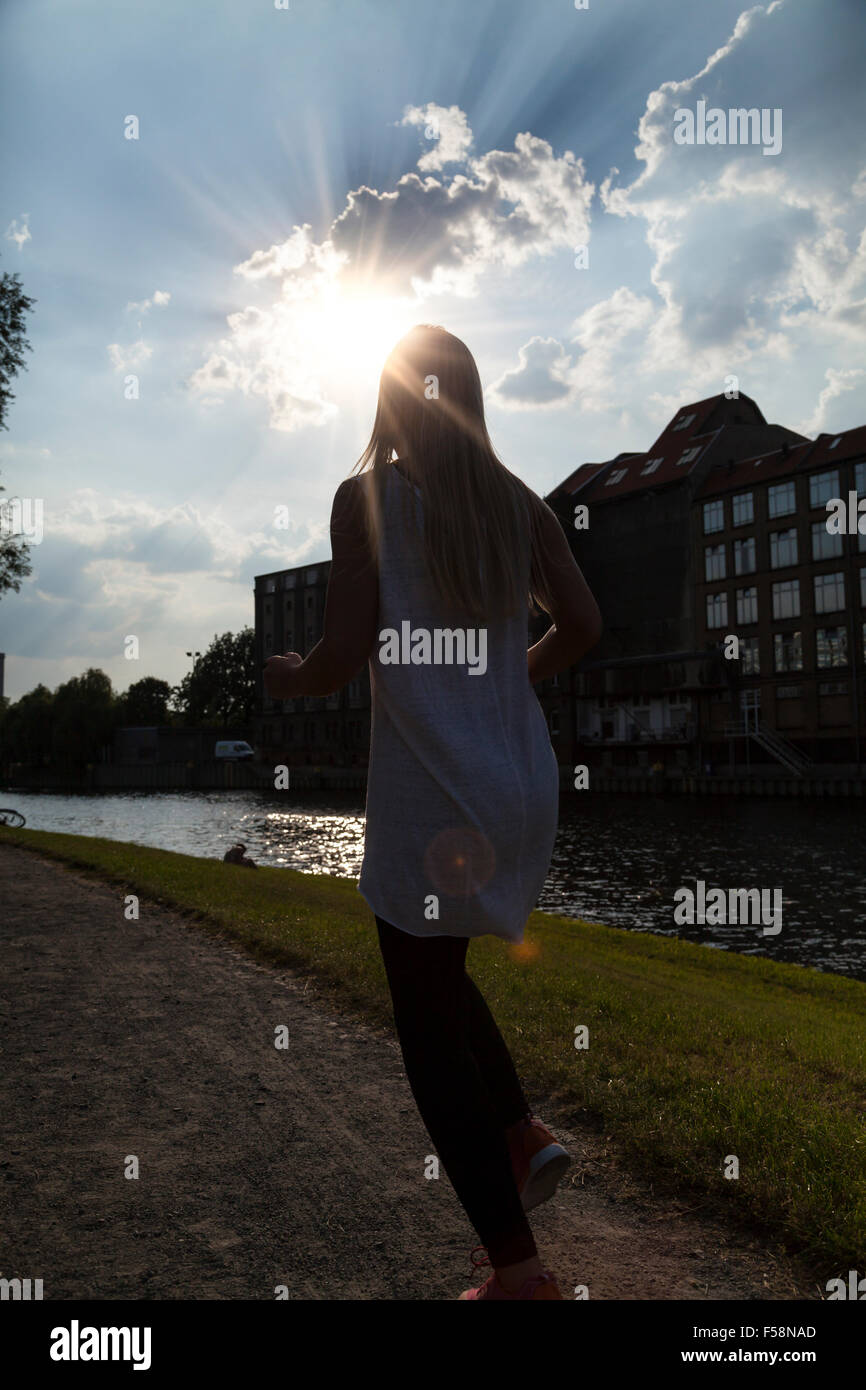 Donna jogging e il sole che tramonta dietro una nuvola Foto Stock