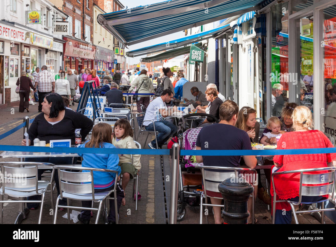 La gente seduta al di fuori di un cafe a mangiare cibo in strada, Skegness, England, Regno Unito Foto Stock
