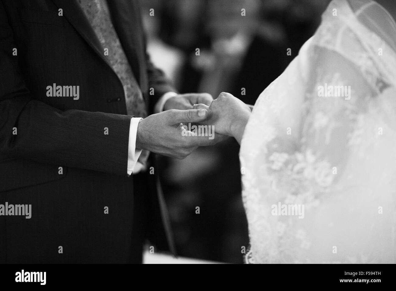 Bianco e nero artistico rettangolare digitale foto orizzontale di mano dello sposo in dark lunga mattinata tuta e camicia bianca con gemelli in chiesa nozze religiose matrimonio cerimonia tenendo le mani per scambiare gli anelli di nozze con la sposa in bianco lungo Foto Stock
