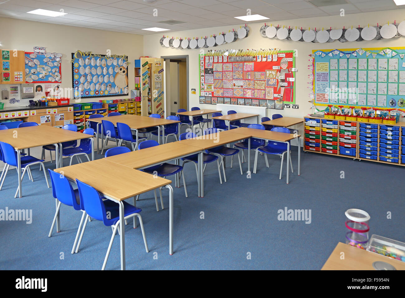 Una classe in una nuova costruzione UK junior school. Mostra scrivania, sedie e colorati cassetti portaoggetti. Bambini arte copre la parete Foto Stock
