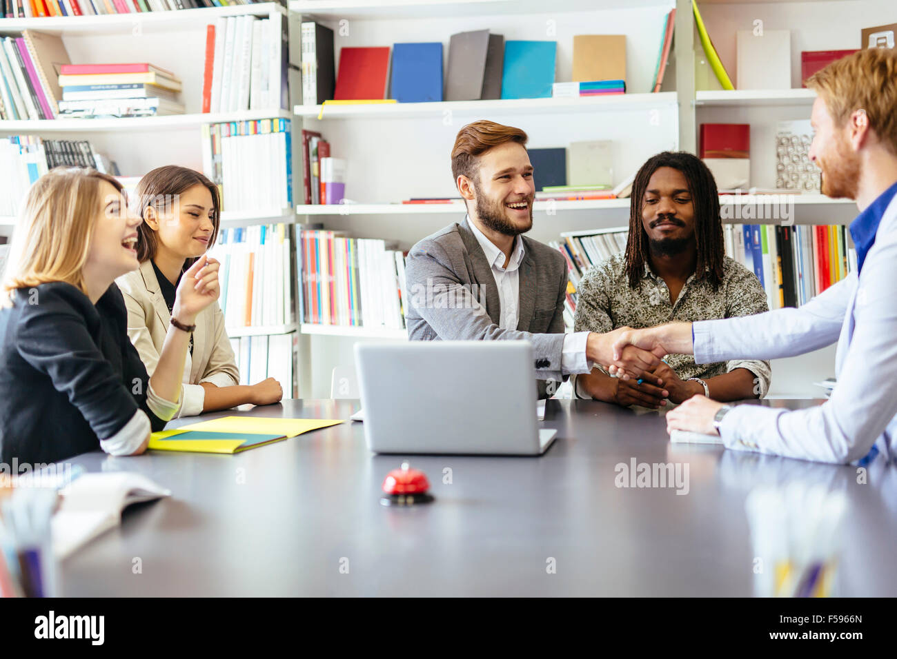 Gli imprenditori si stringono la mano in ufficio con i colleghi e lo staff di sedere a tavola con loro Foto Stock