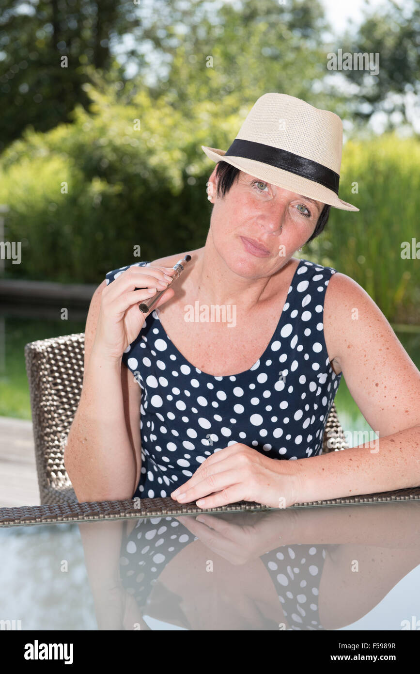 Donna attraente siiting presso la piscina e il fumo e-sigaretta Foto Stock