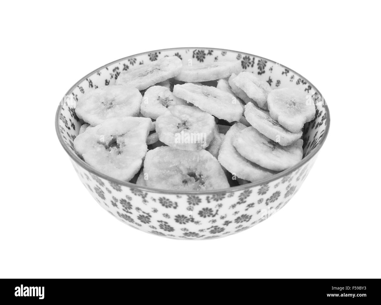 Banane essiccate chip in un vaso di porcellana con un design floreale, isolata su uno sfondo bianco - elaborazione monocromatica Foto Stock