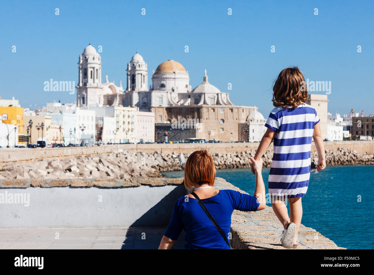 I turisti madre e figlia con strisce blu t shirt sul lungomare con la cattedrale di Cadice, Andalusia, Spagna Foto Stock
