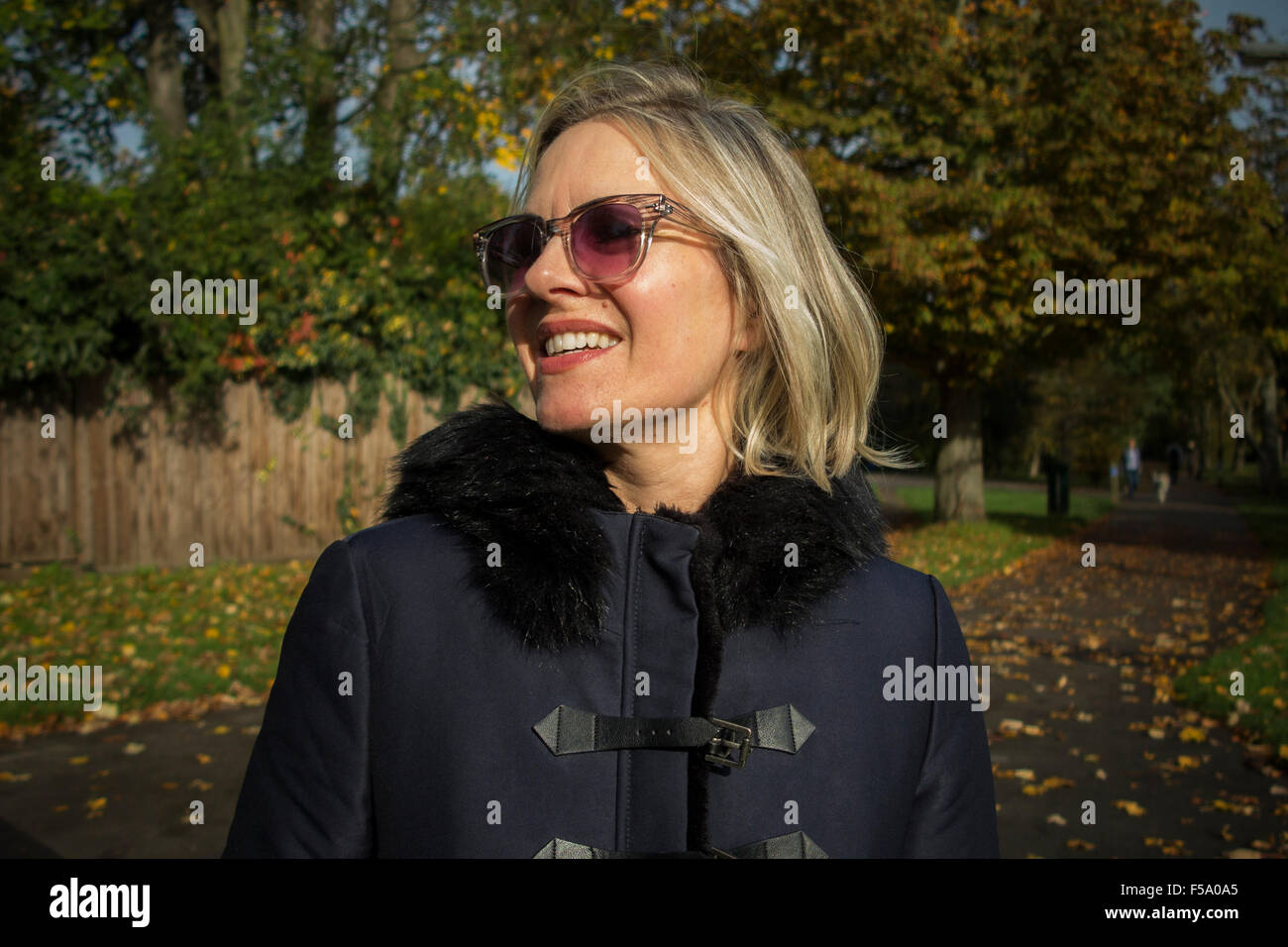 Gode di una donna il sole autunnale su una passeggiata in un parco di Londra Foto Stock Gode di una donna il sole autunnale su una passeggiata in un parco di Londra Foto Stock