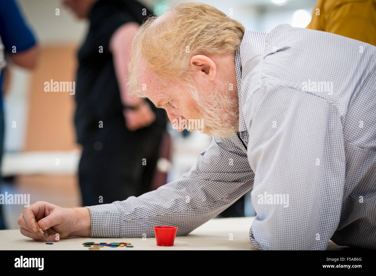 Cambridge, Regno Unito. Il 31 ottobre, 2015. Un concorrente prende un colpo in inglese Tiddlywinks coppie nazionali campionati che si svolgono presso Selwyn College di Cambridge Regno Unito. Lungi dall essere un gioco da bambini, la concorrenza è un mix di strategia e destrezza per la propulsione della "winks" utilizzando un "squidger" in una pentola o per coprire gli avversari "winks". La nascita del moderno gioco può essere ricondotto a un gruppo di Cambridge (UK) laureandi in 1955. Credito: Julian Eales/ Alamy Live News Foto Stock