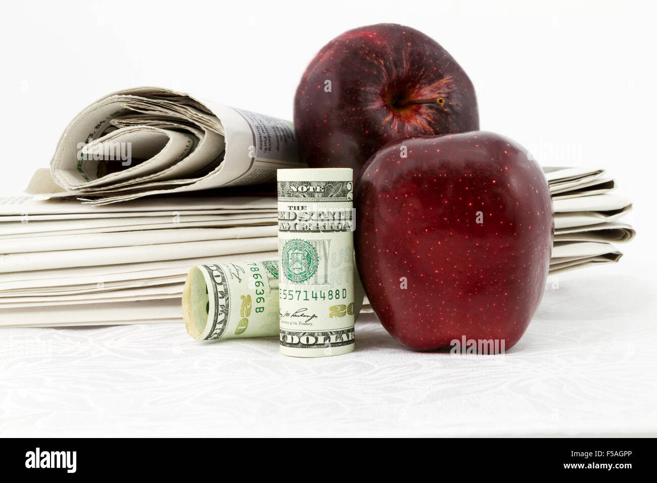 Due mele e moneta americana collocato con la pila di quotidiani riflettere notizie e informazioni sui legami di istruzione e finanze. Foto Stock