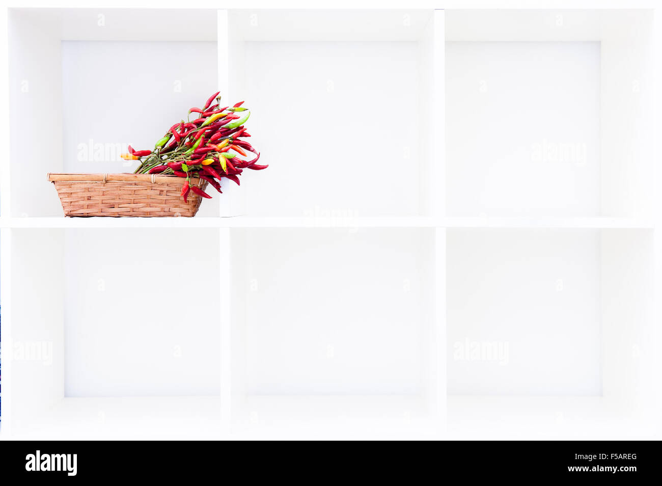 Mazzetto di pepe rosso in marrone cesto su cubico scaffale bianco con spazio di copia Foto Stock