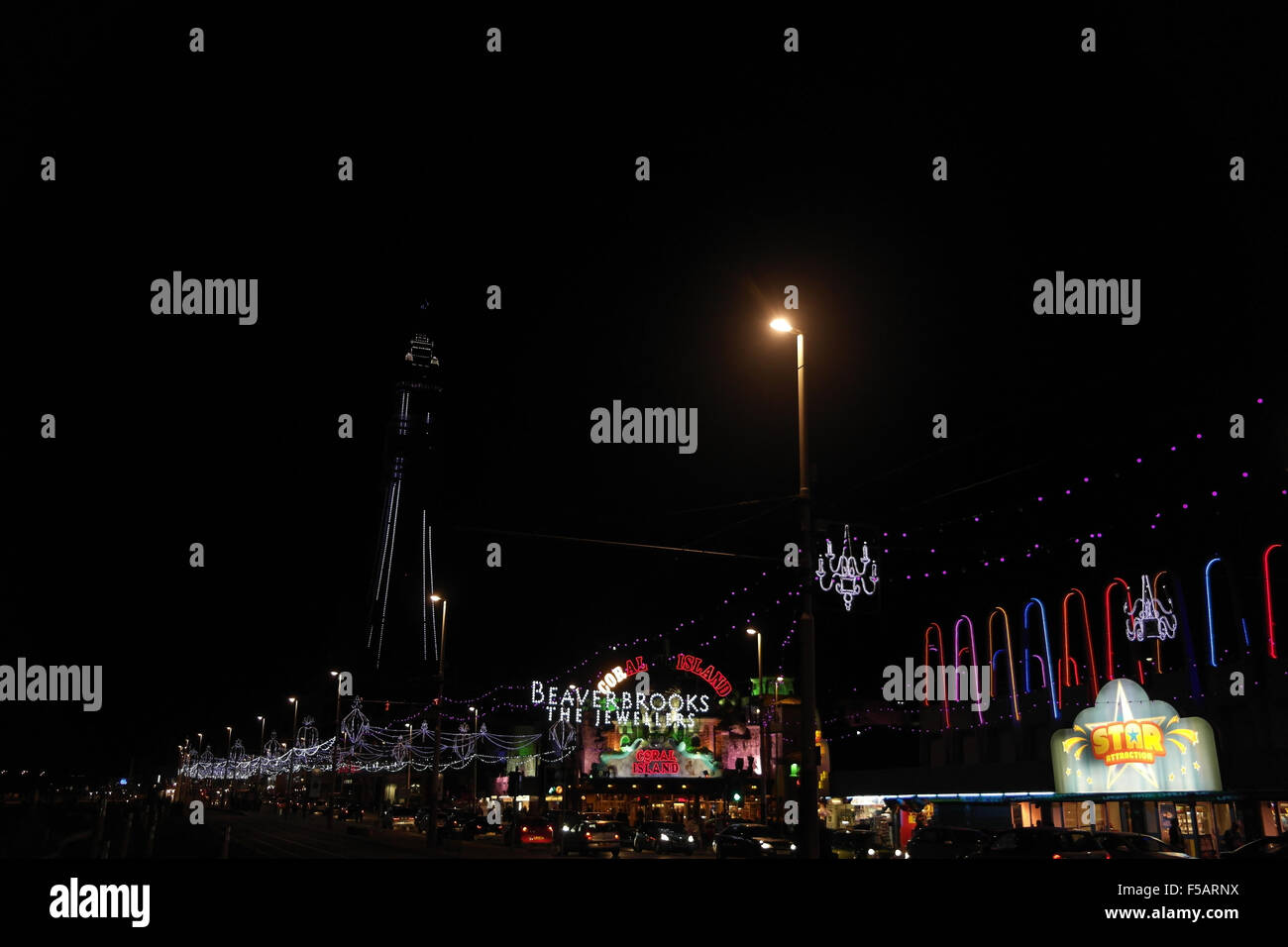Notte vista obliqua il traffico lungo la Central Promenade di attrazione a Bling luminarie e illuminata dalla torre di Blackpool, Regno Unito Foto Stock