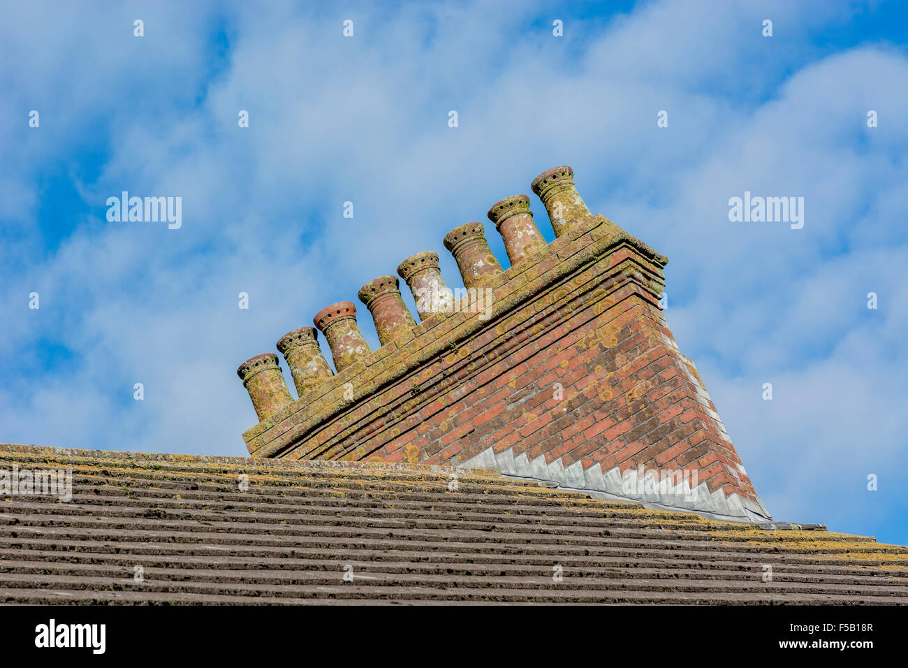 Colpo 'scheggiato' di una fila di pentole domestiche del camino regolato contro un cielo blu e nuvoloso. Per il settore edile del Regno Unito. Foto Stock