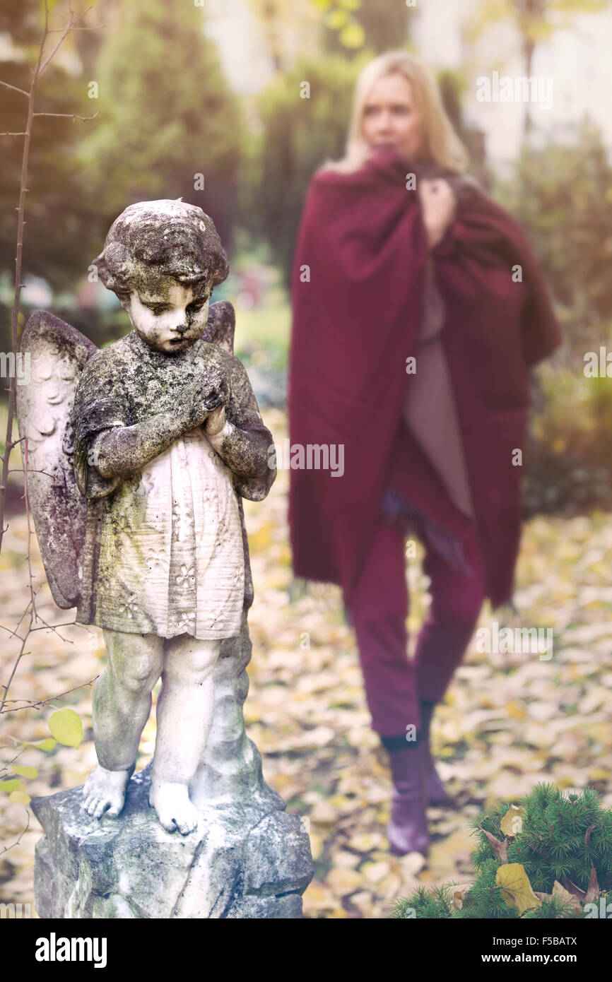 Donna che cammina nel cimitero accanto alla statua di little angel Foto Stock