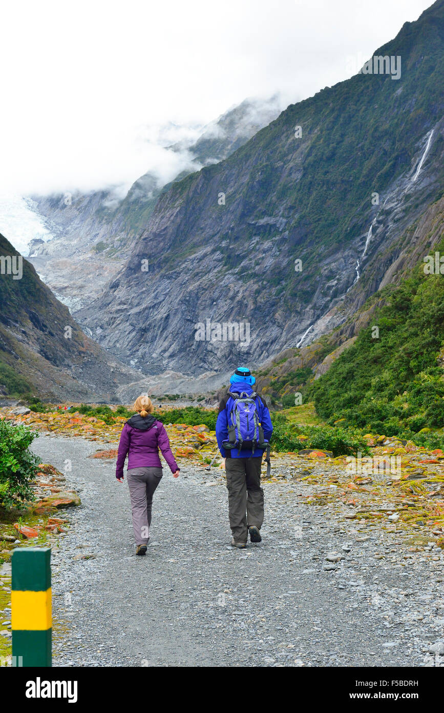 Due escursionisti che camminano lungo un percorso roccioso lungo il fiume vicino al ghiacciaio fondono l'acqua fino alla Toe dell'Isola Sud del ghiacciaio Franz Josef, Nuova Zelanda Foto Stock