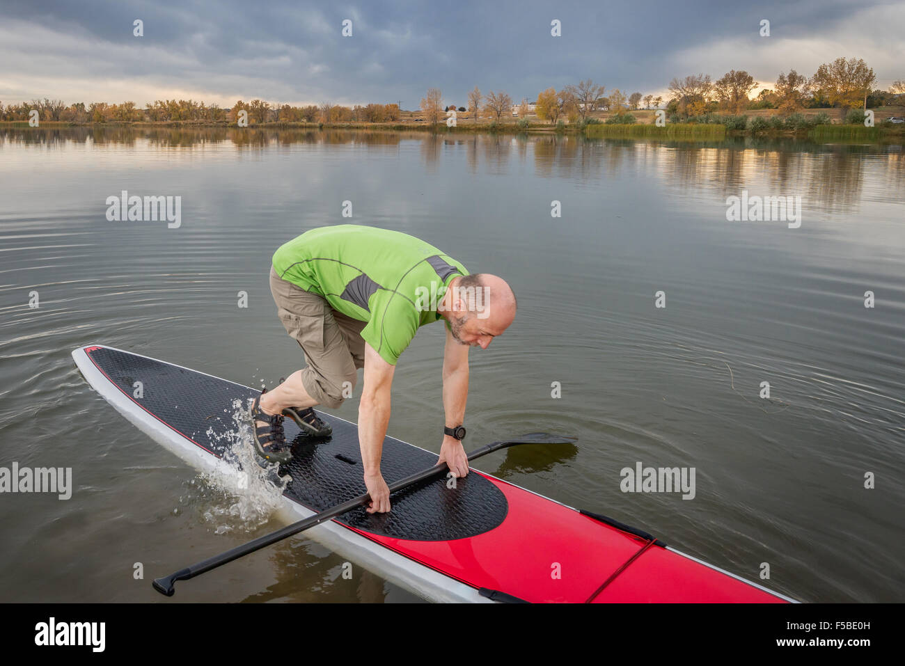 Senior maschio è a partire paddling allenamento sul suo stand up paddleboard sulle sponde di un lago in Colorado Foto Stock