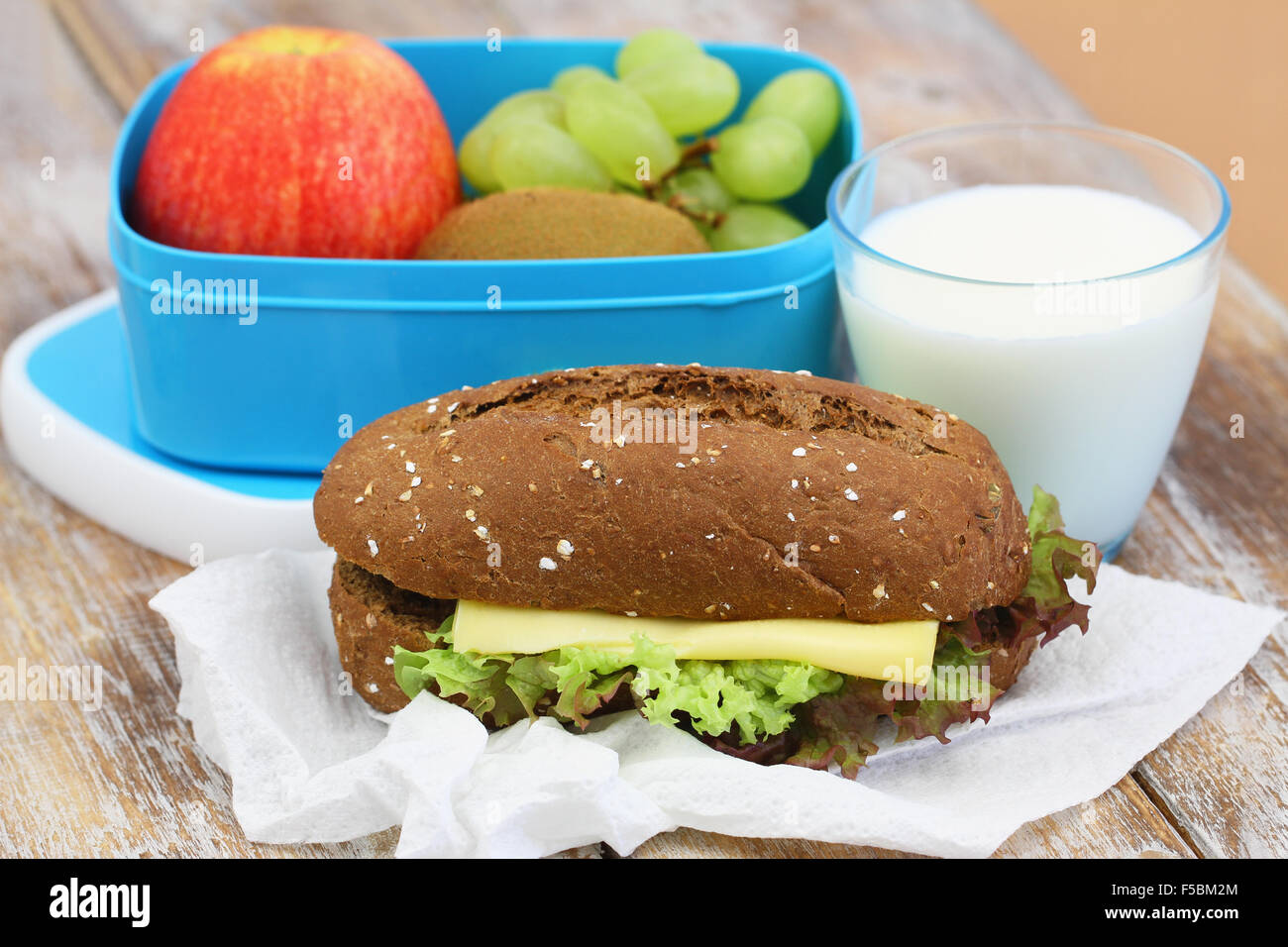 Marrone sandwich di pane con formaggio e lattuga e scatola di pranzo pieno di frutta fresca Foto Stock