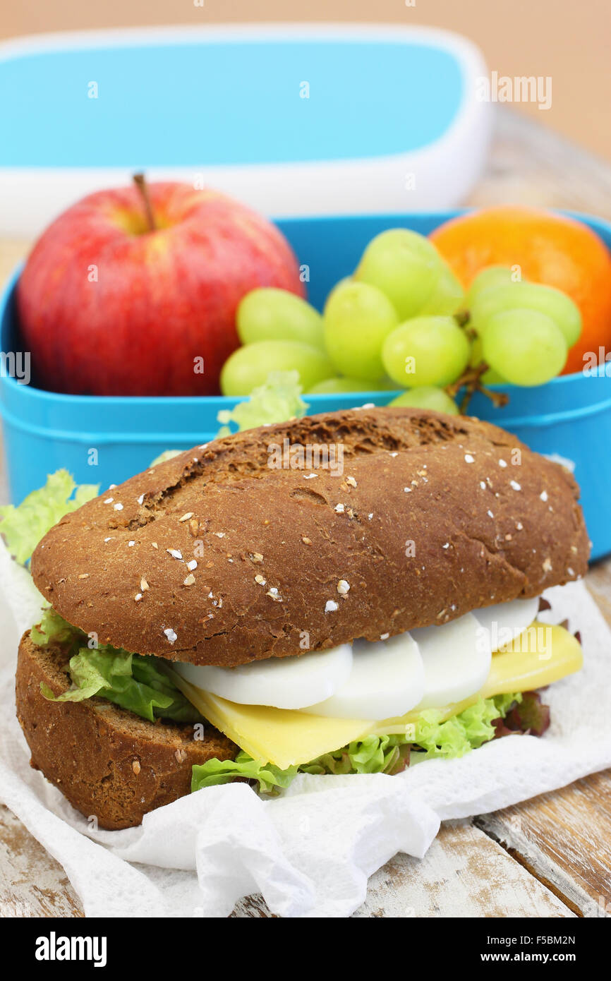 Marrone sandwich di pane con formaggio, uovo sodo e lattuga e scatola di pranzo pieno di frutta fresca Foto Stock