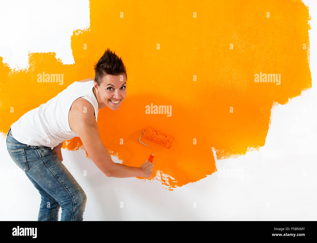 Bella Donna informale di verniciatura di un muro bianco con colore arancione. Lei sta cercando la fotocamera con un sorriso amichevole. Foto Stock