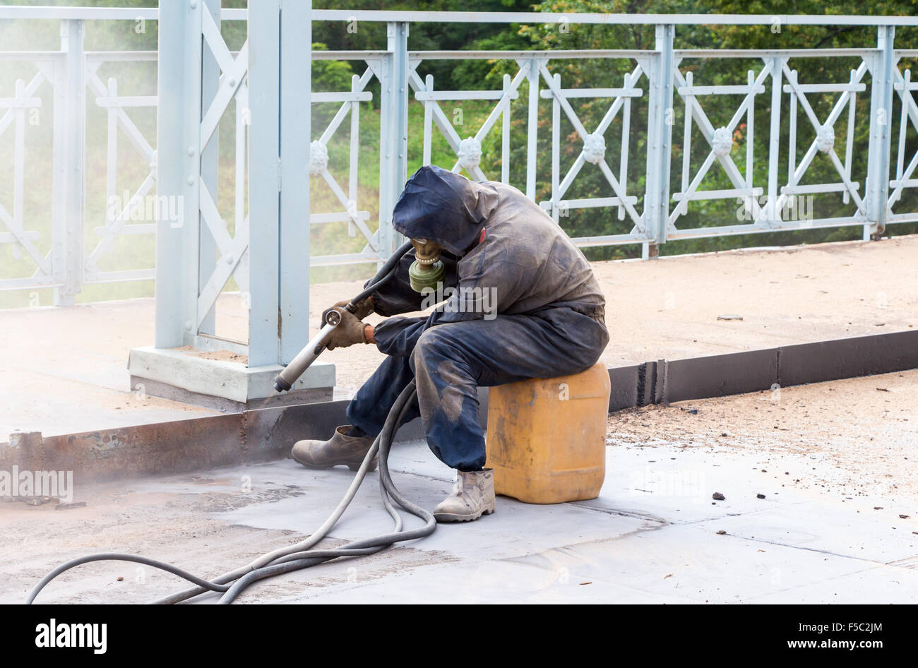 Lavoratore in indumenti protettivi pulisce le strutture metalliche strumento di sabbiatura Foto Stock