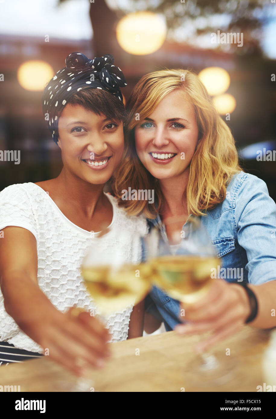 Divertimento attraente giovane femmina amici celebrando con vino bianco tintinnio loro bicchieri in un brindisi come hanno sorriso a thecamera, mu Foto Stock