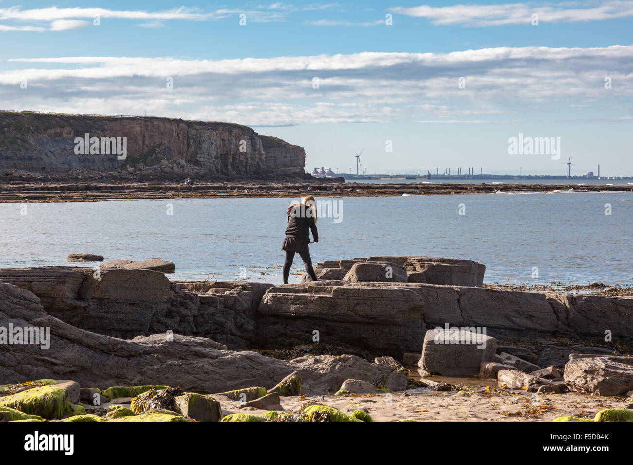 Una donna sulle rocce vicino a seaton sluice scatta una fotografia con un telefono cellulare, il porto di Blyth è in distanza, Tyne and Wear, Regno Unito Foto Stock