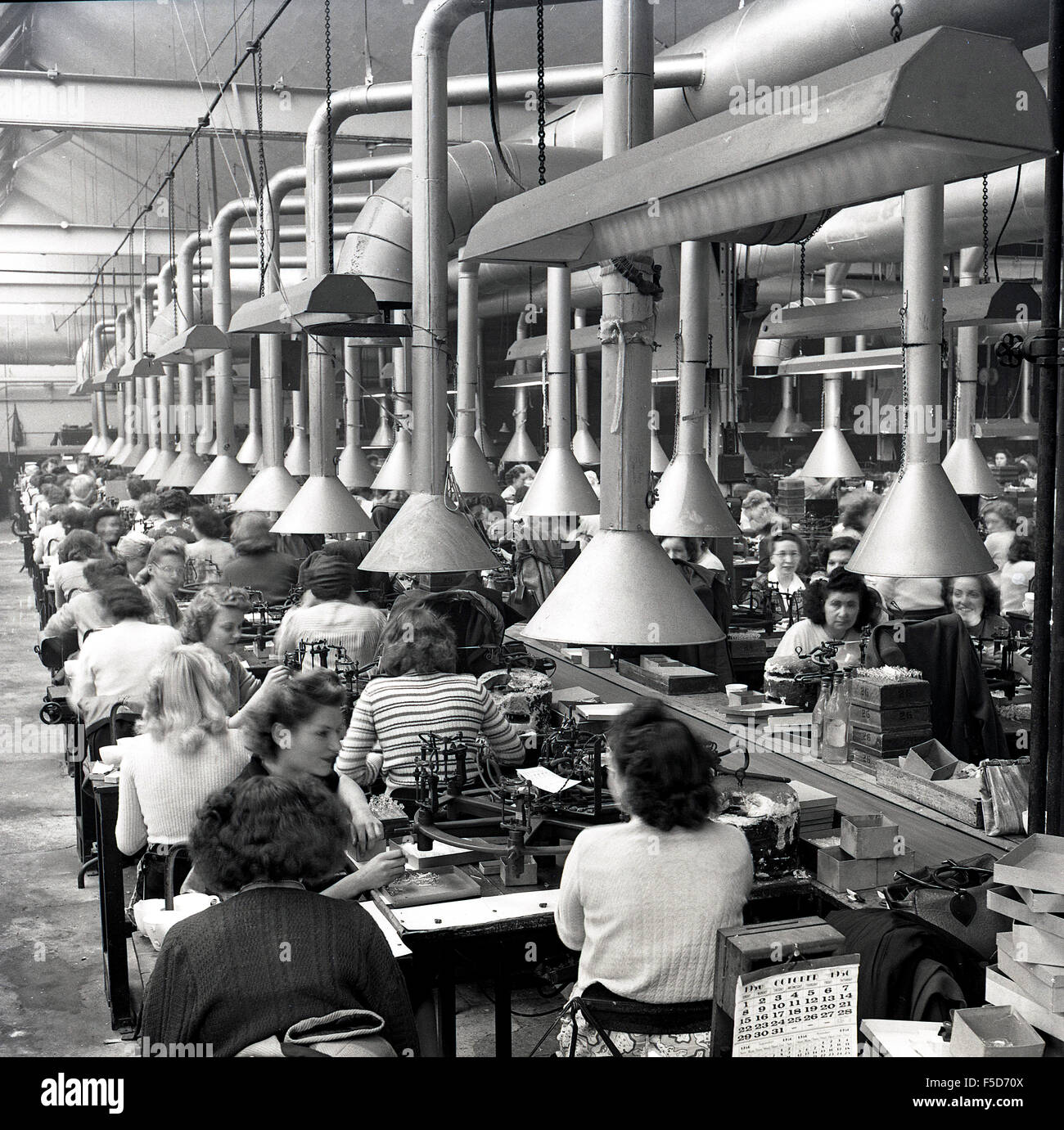 Ottobre 1950 e vista storica di righe delle donne al lavoro in una fabbrica di linea di produzione. Foto Stock