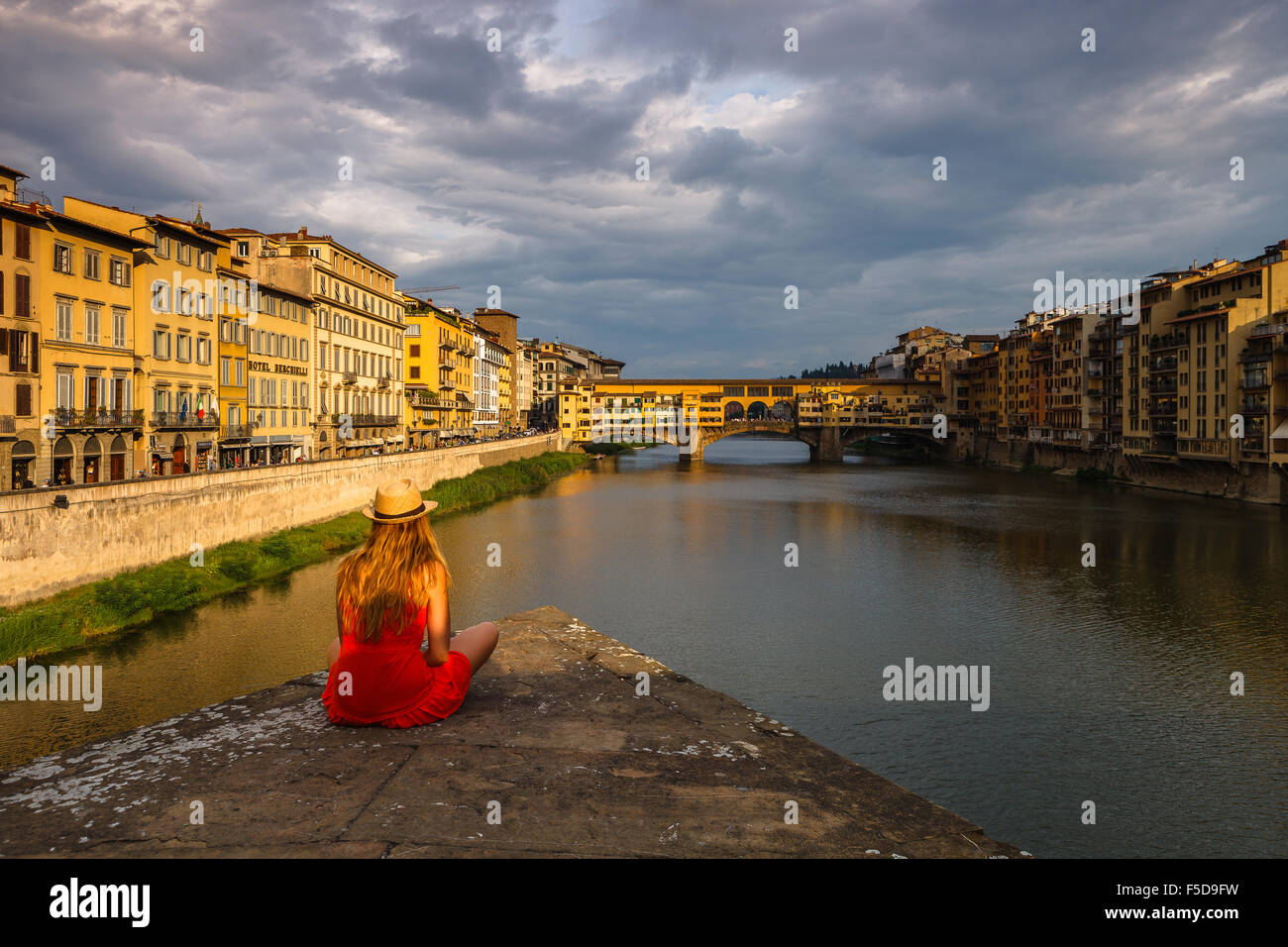 Una giovane donna godendo la vista del Ponte Vecchio e sul fiume Arno dal tramonto, Firenze, Toscana, Italia. Foto Stock