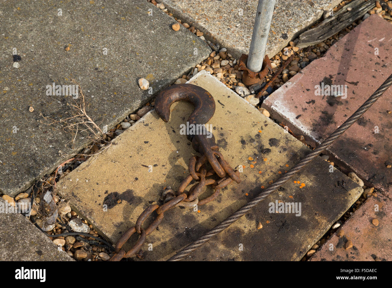 Grande gancio in metallo in appoggio sulla lastra di pavimentazione con un twisted metal cavo a spirale e la catena Foto Stock