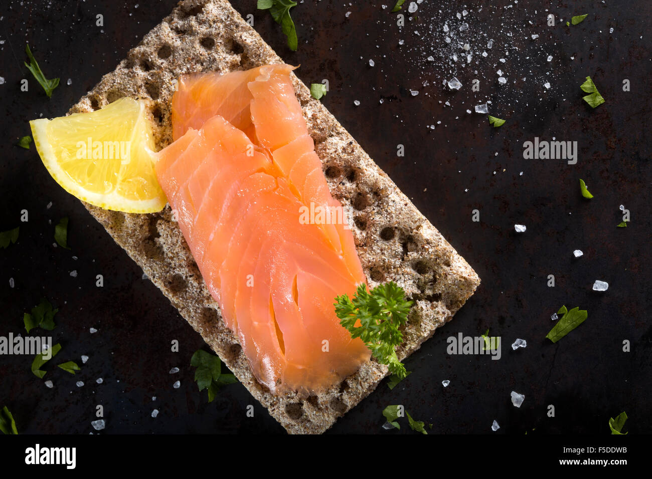 Salmone affumicato su cracker integrale con il prezzemolo, limone e sale Foto Stock