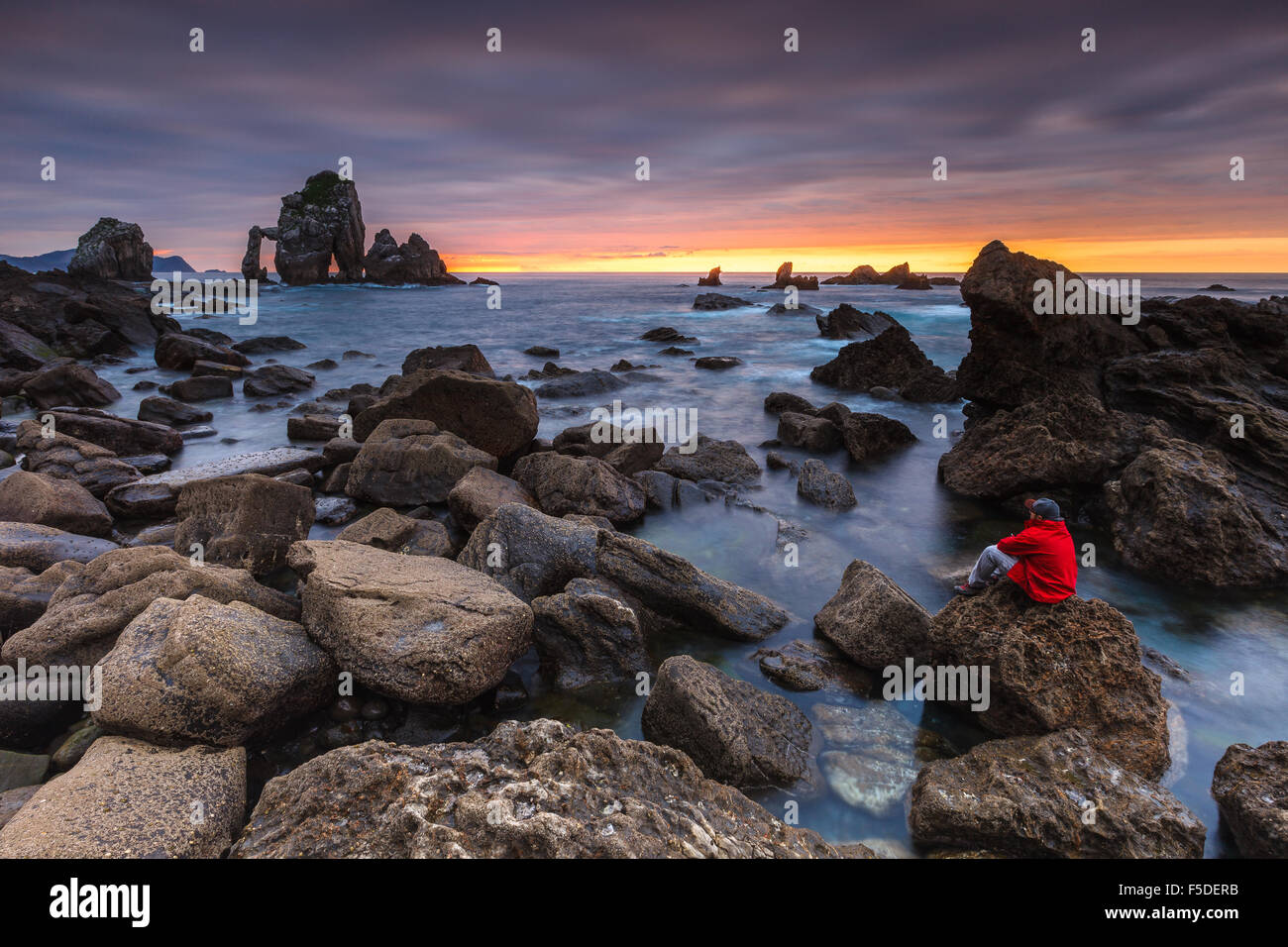 Un giovane uomo ammirando la costa rocciosa di San Juan de Gaztelugatxe, Vizcaya, Paesi Baschi. Foto Stock