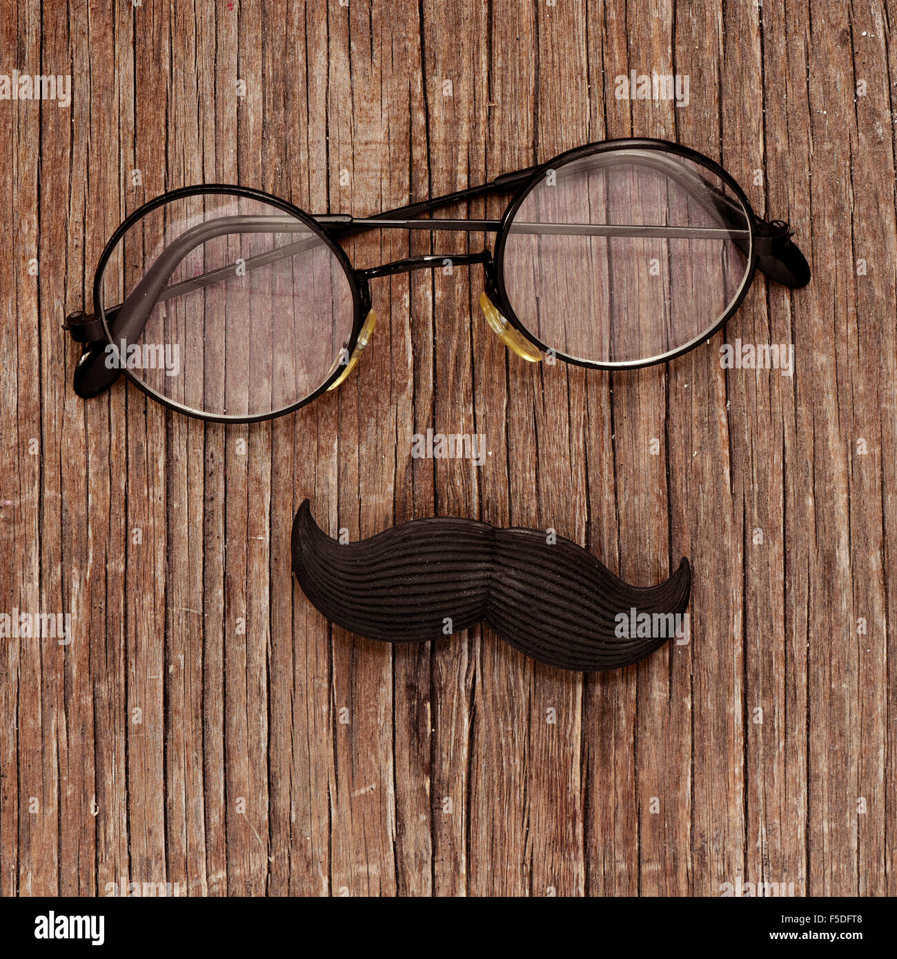 Una coppia di round-incorniciato occhiali e baffi finti su un rustico di  superficie in legno raffigurante un uomo faccia Foto stock - Alamy