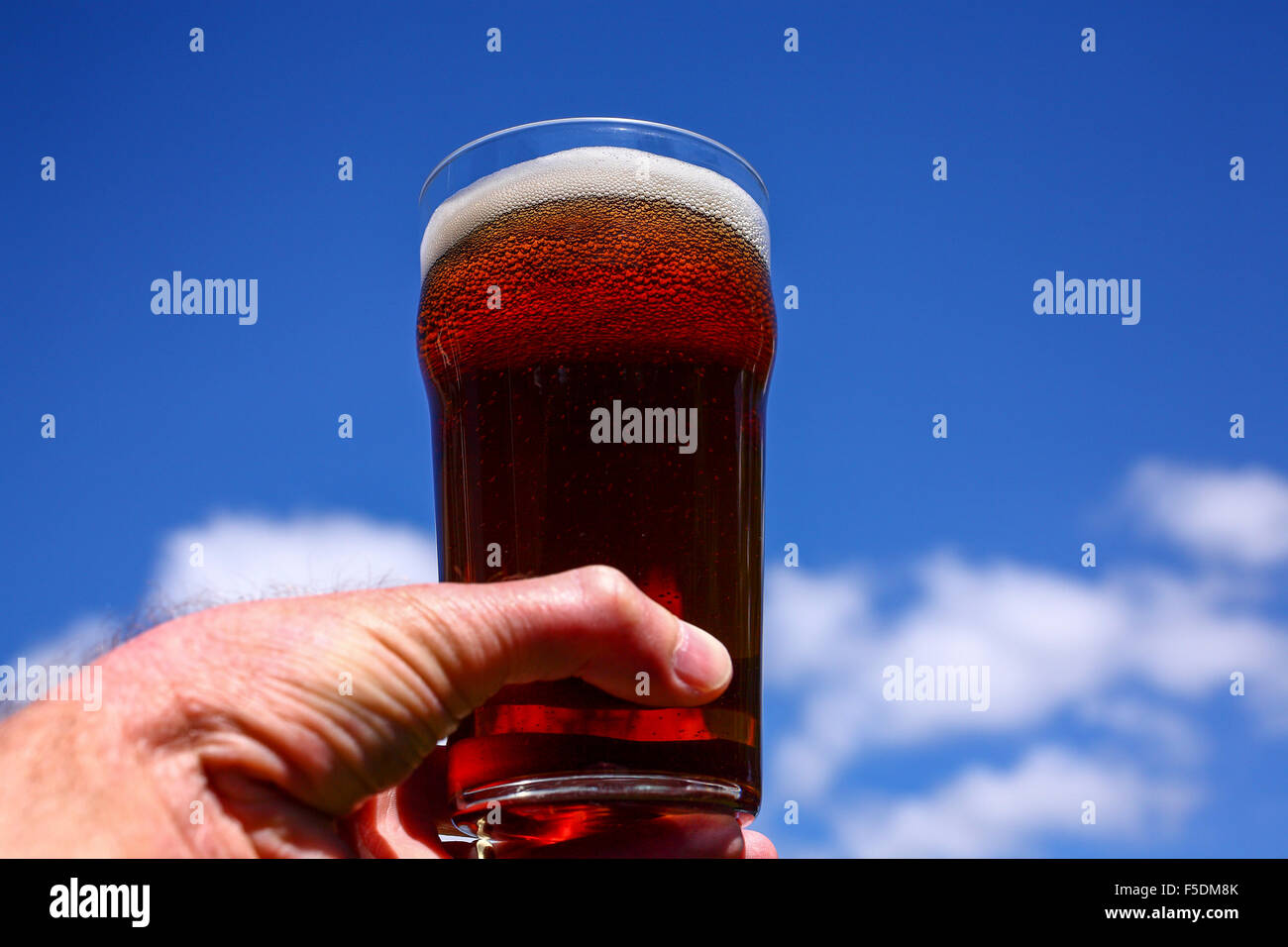 Man mano che tiene una pinta bicchiere di birra amara contro un Cielo di estate blu Foto Stock