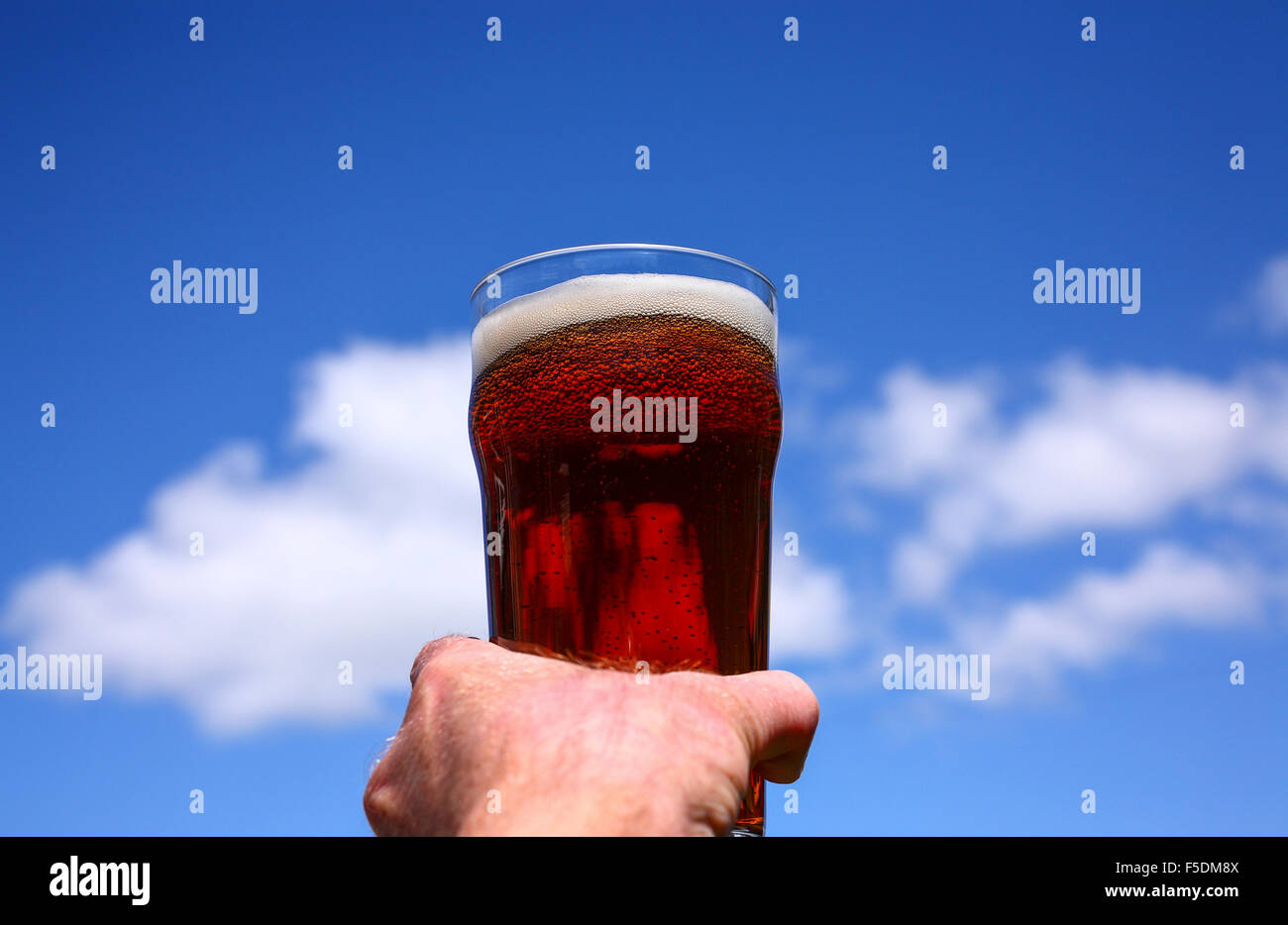 Man mano che tiene una pinta bicchiere di birra amara contro un Cielo di estate blu Foto Stock