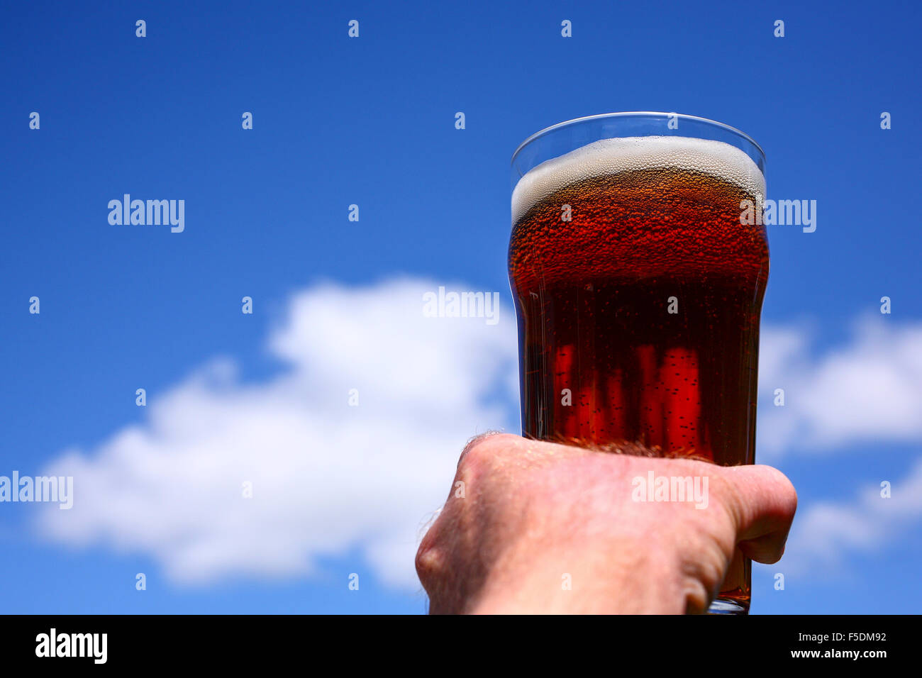 Man mano che tiene una pinta bicchiere di birra amara contro un Cielo di estate blu Foto Stock